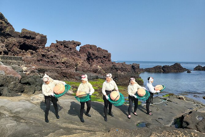 Jeju haenyeo divers in white wetsuits holding round net floats on volcanic rocks by the sea
