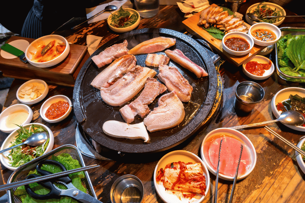 Jeju black pork belly grilling on a round griddle surrounded by banchan side dishes