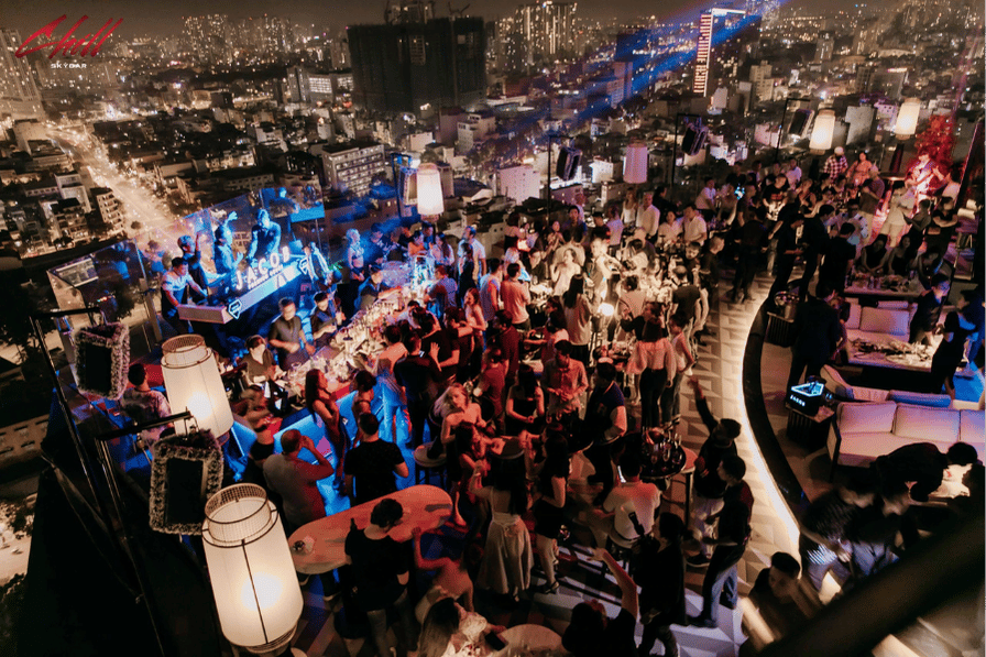 A crowded rooftop bar at night overlooking Ho Chi Minh City's lit-up skyline