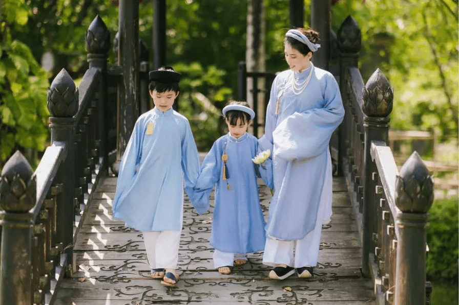 A woman and two children in traditional ao dai crossing a garden bridge