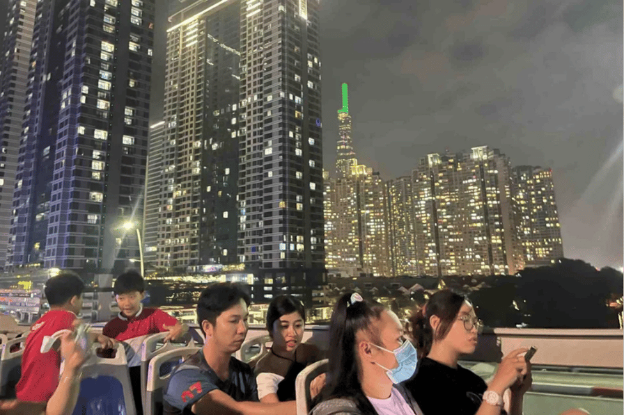 Passengers on an open-top night bus with Ho Chi Minh City's lit skyline behind