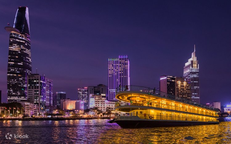 An illuminated cruise boat on the Saigon River at night with the skyline behind