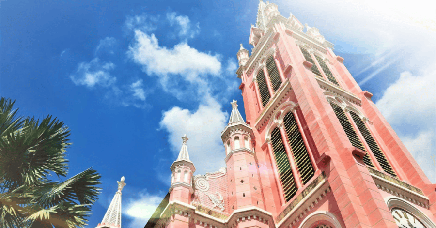 The candy-pink spire of Tan Dinh Church against a blue sky with a palm tree