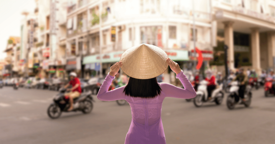 A woman in a purple ao dai crossing a busy Saigon street full of motorbikes