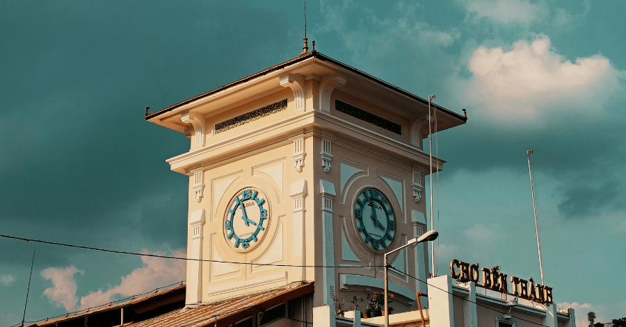 The iconic yellow clock tower of Ben Thanh Market against a moody sky
