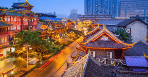 Traditional Chinese architecture lit gold at dusk with Chengdu's modern skyline behind