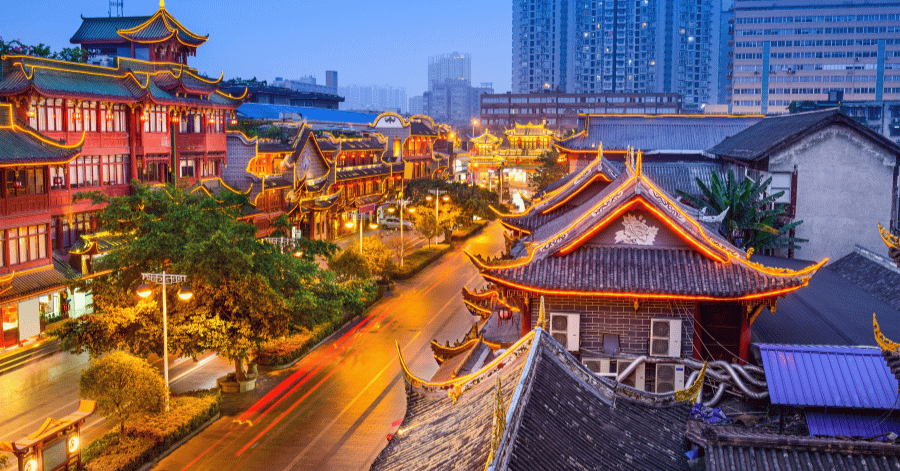 Traditional Chinese architecture lit gold at dusk with Chengdu's modern skyline behind