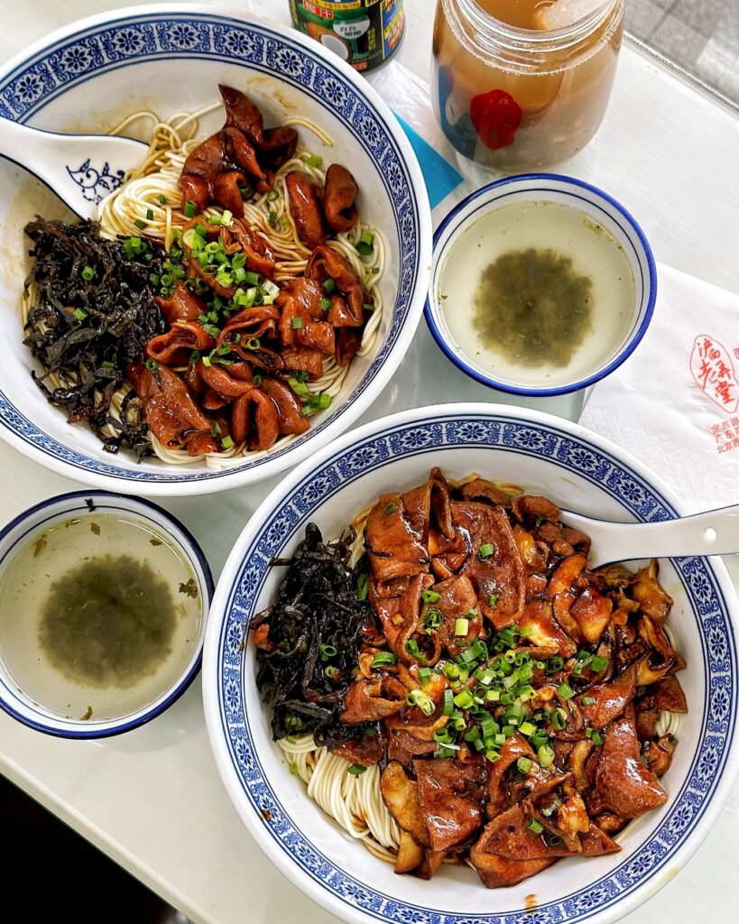 Two bowls of noodles topped with braised pork and spring onion in blue-rimmed bowls