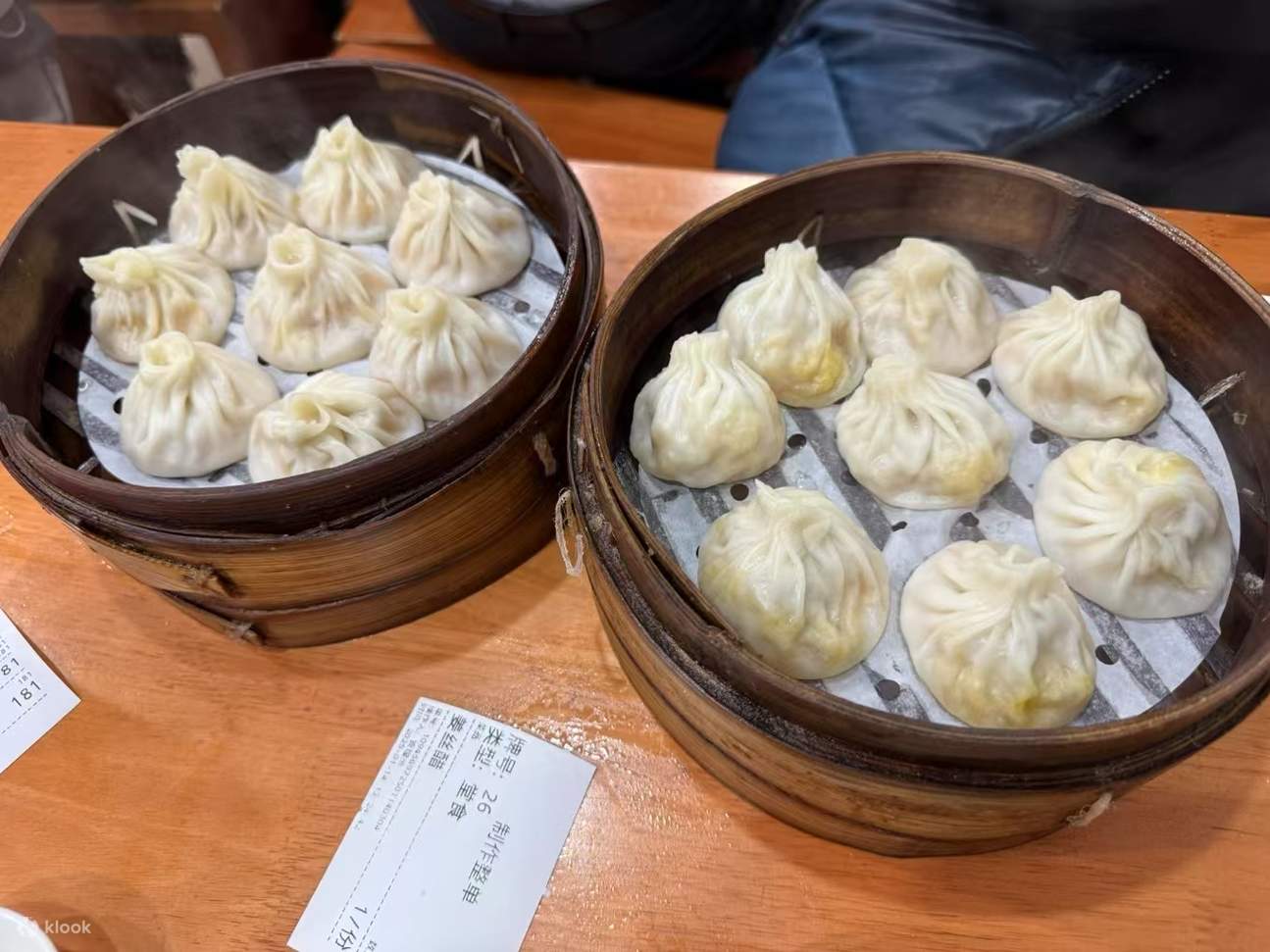 Two bamboo steamers of pleated xiaolongbao soup dumplings on a wooden table