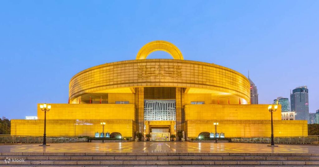 The golden, round-topped Shanghai Museum building lit at dusk on People's Square