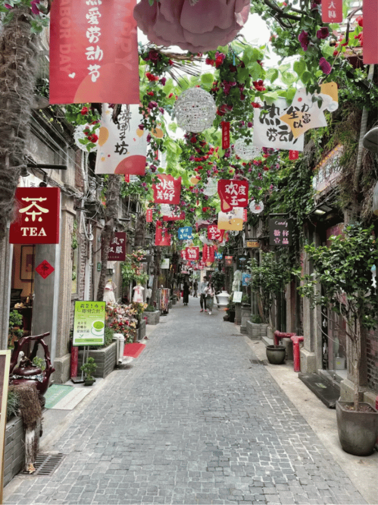 A narrow Shanghai lane hung with red decorations and lined with small shops and a tea sign