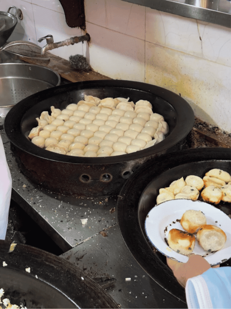 A round griddle of crispy-bottomed pan-fried pork buns at a Shanghai shop