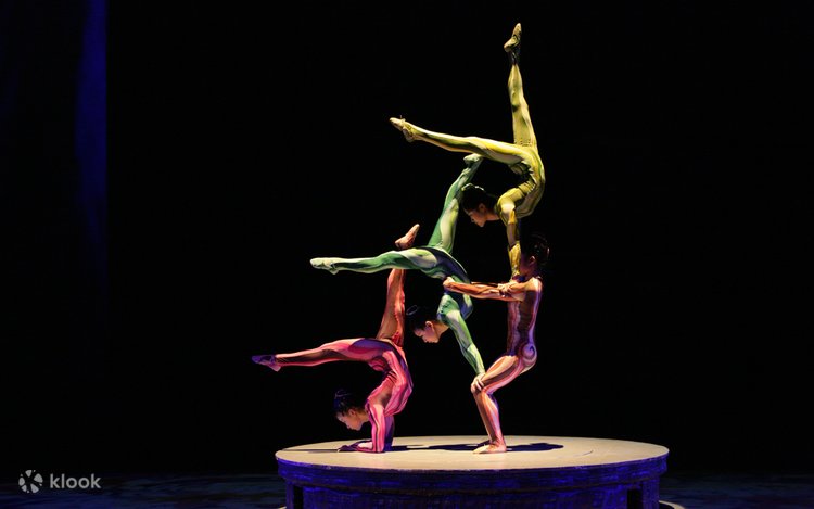 Three costumed acrobats balancing in a stacked pose under stage lights at a Shanghai show