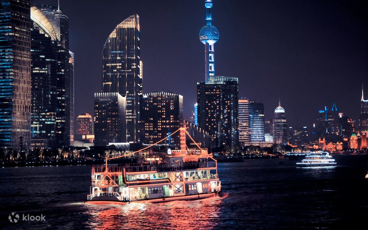 A lit pleasure boat cruising the Huangpu River at night with Shanghai's Pudong skyline behind