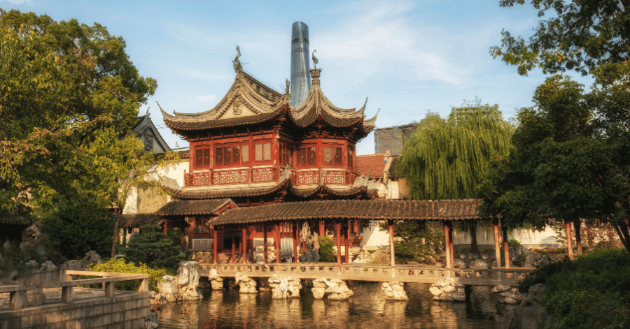 A classical red-and-grey pavilion beside a pond in Shanghai's Yu Garden, framed by willow