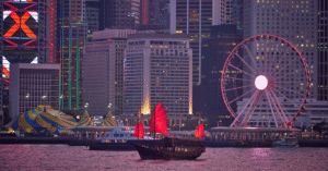 Hong Kong's Victoria Harbour at dusk with a red-sail junk boat and the Observation Wheel against the skyline