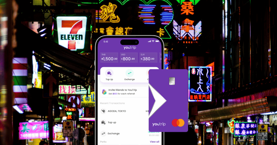 Smartphone showing the YouTrip app held against a neon-lit Hong Kong street with a 7-Eleven at night