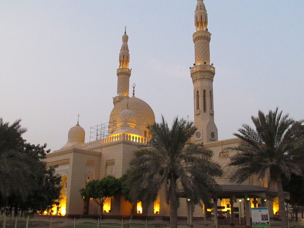 Jumeirah Mosque's twin minarets and central dome lit at dusk behind palm trees