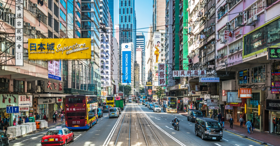 Busy Hong Kong street with double-decker buses, trams and shop signs between high-rise buildings