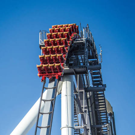 A roller coaster train cresting a steep climb against a clear blue sky