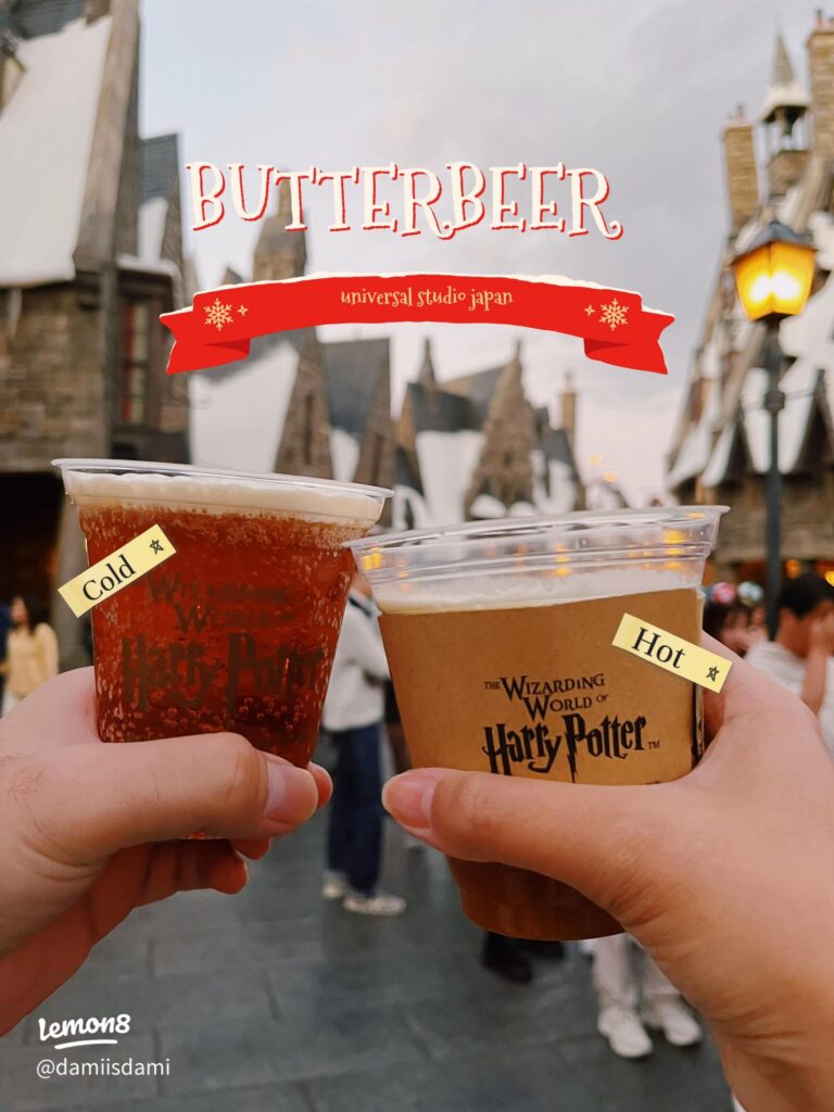 Two cups of Butterbeer, one cold and one hot, held up in front of Hogsmeade