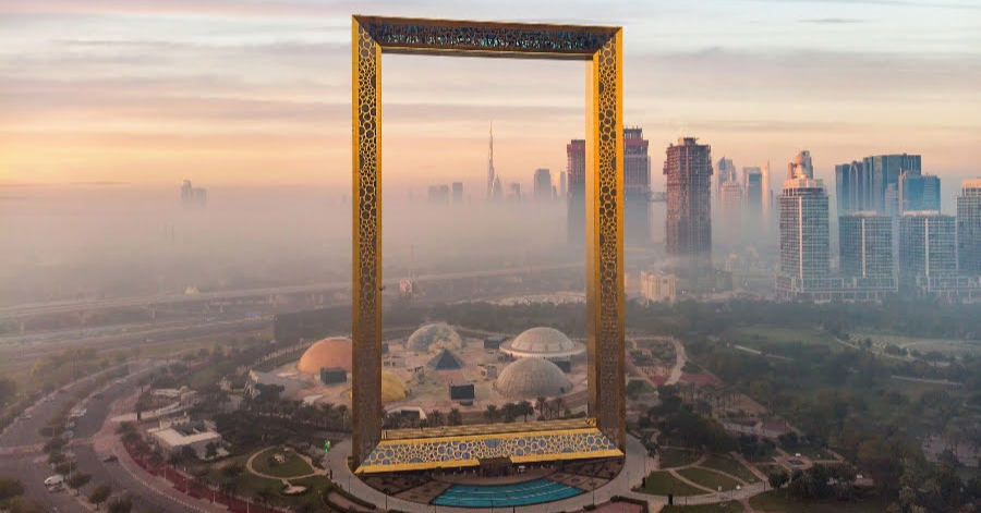The golden rectangular Dubai Frame standing over parkland at sunrise