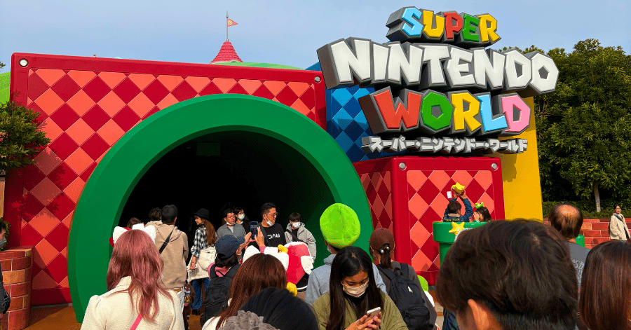 Crowds entering Super Nintendo World through the giant green warp-pipe tunnel under the colourful sign
