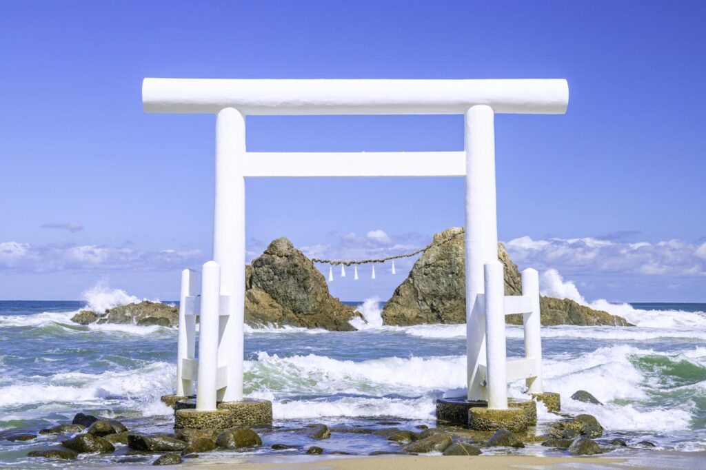 A white seaside torii gate framing the Sakurai Futamigaura couple rocks amid crashing waves in Itoshima