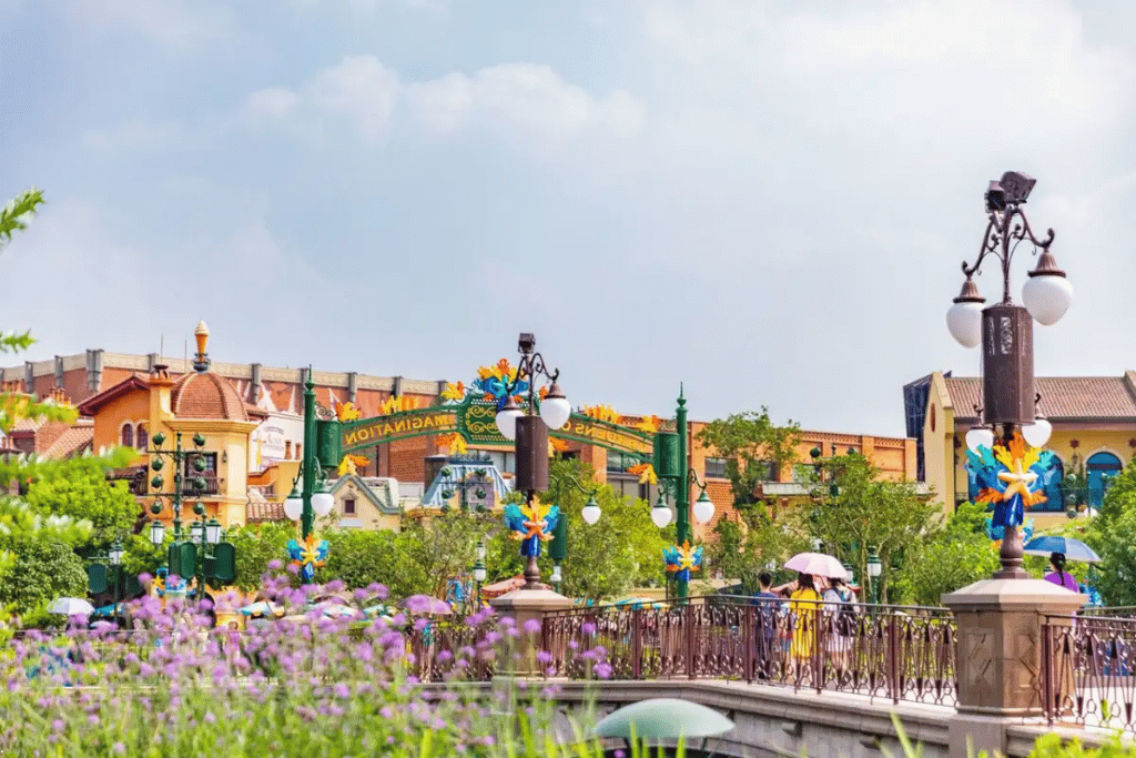 A footbridge and lamp posts leading into the Gardens of Imagination at Shanghai Disneyland, with flowers in the foreground