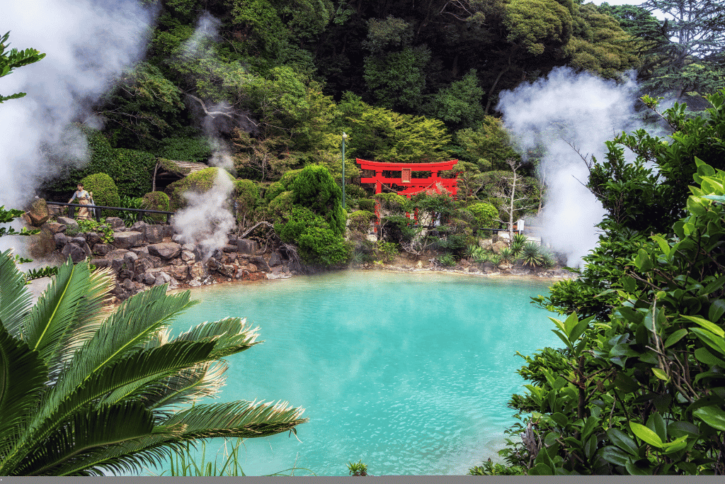 The turquoise, steaming Umi Jigoku hot spring with a red torii amid greenery at Beppu