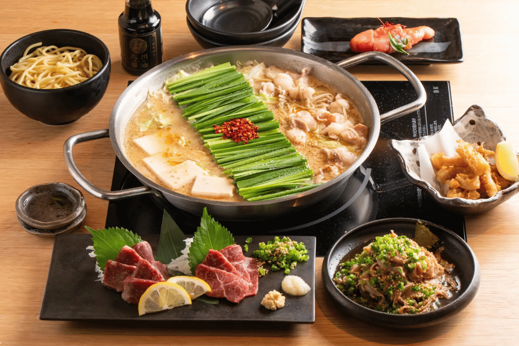 A motsunabe offal hotpot with garlic chives, tofu and side dishes laid out on a table
