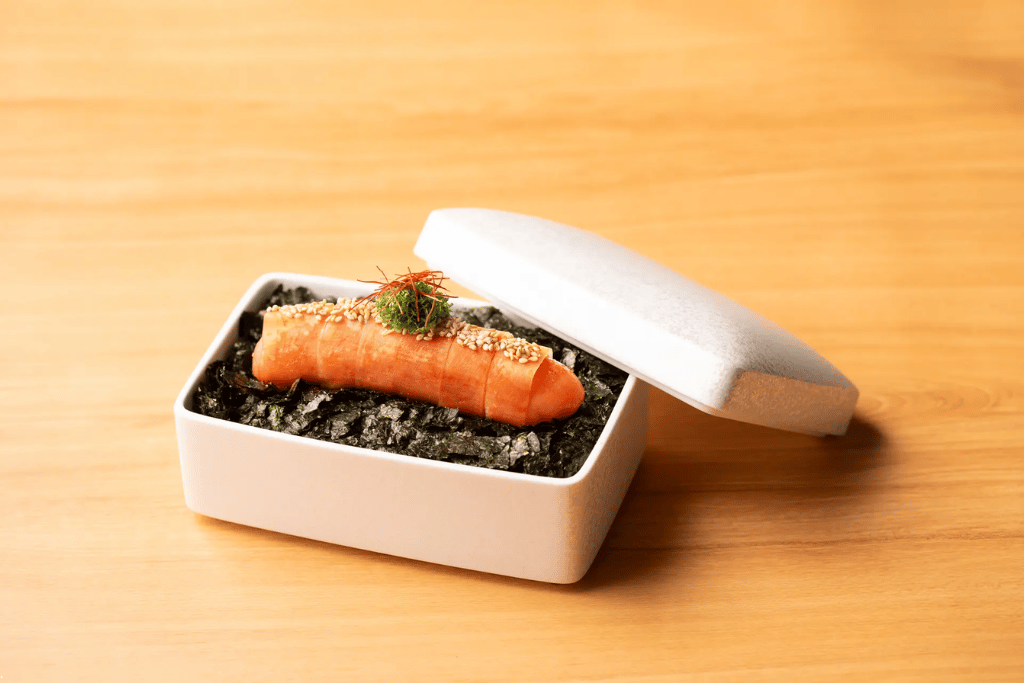 A piece of mentaiko spicy cod roe presented in a white box over shredded nori