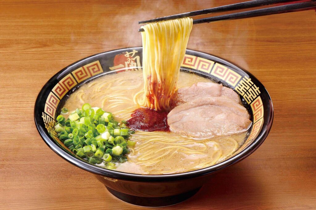 A steaming bowl of Ichiran tonkotsu ramen with chashu pork, spring onions and noodles lifted by chopsticks