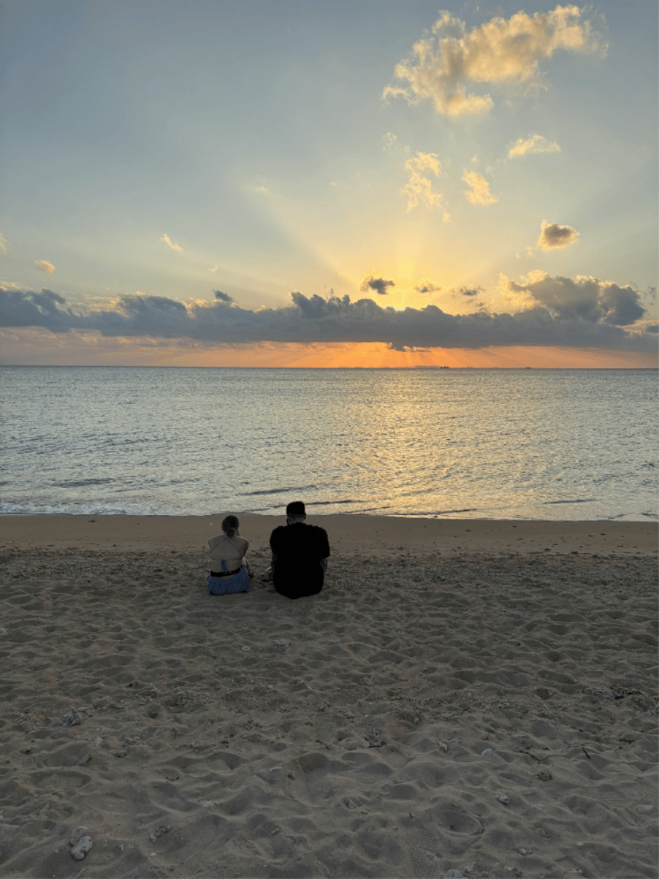 Couple sitting on the sand watching the sun set over the ocean in Okinawa