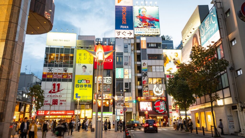 A busy Tenjin street at dusk lined with shops, neon billboards and pedestrians in central Fukuoka