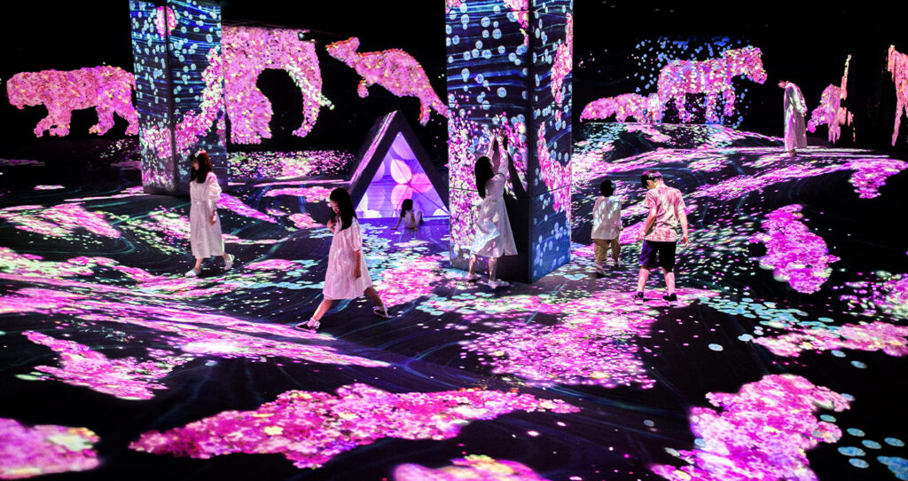 Glowing pink projected animals and flowers surrounding visitors at teamLab Forest, Fukuoka