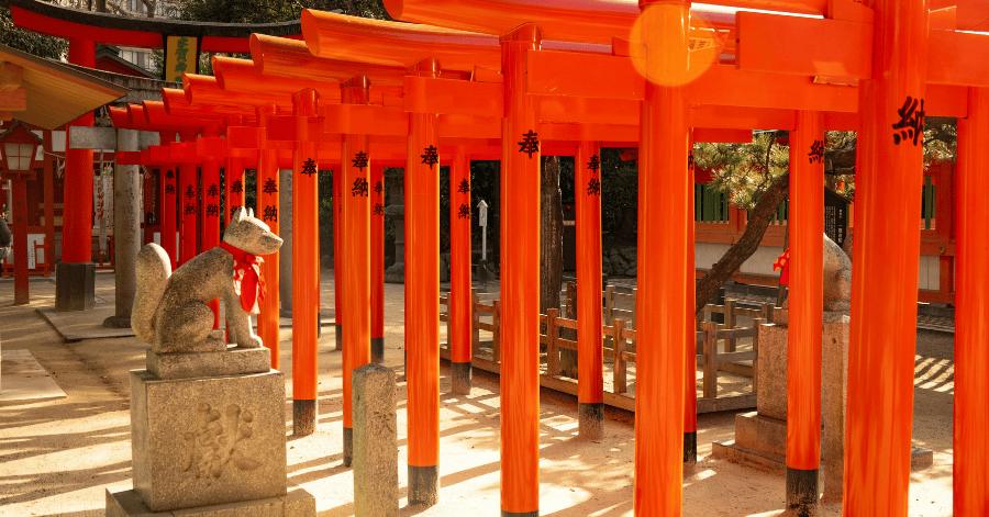 A tunnel of vermilion torii gates with a stone guardian fox statue at a Fukuoka shrine
