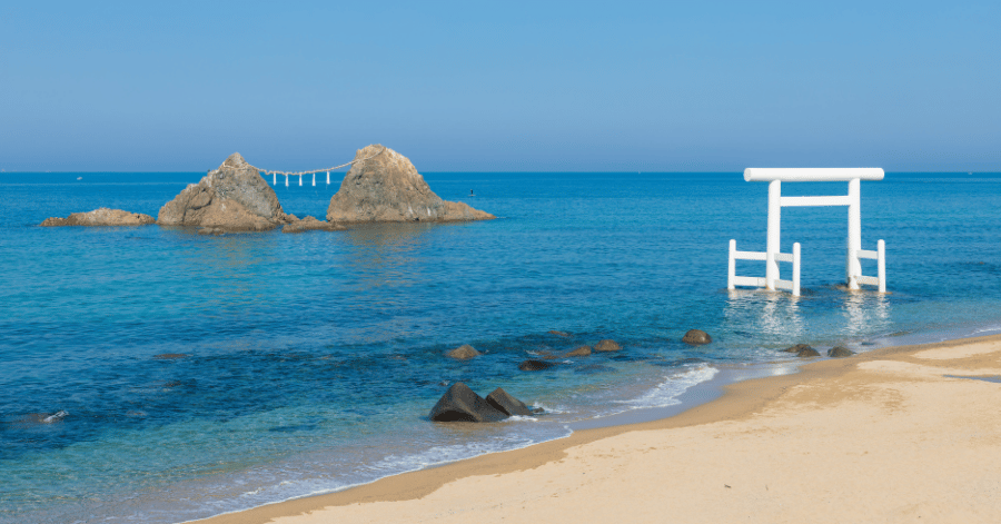 Two sacred rocks joined by a rope beside a white torii gate in the sea at Sakurai Futamigaura, Itoshima