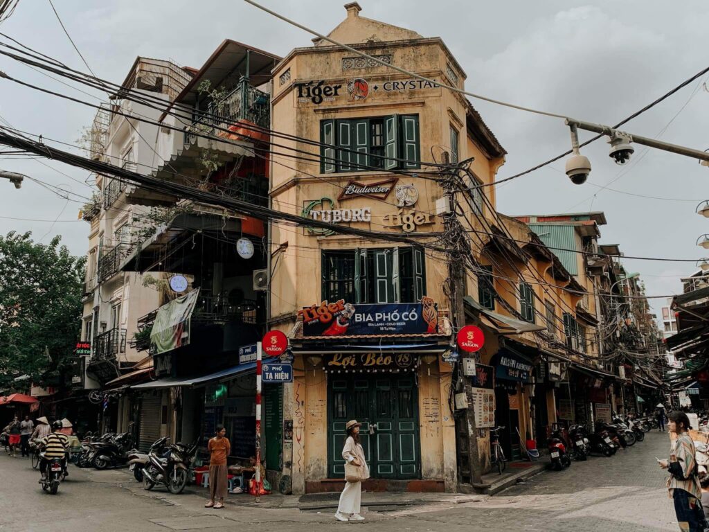 Narrow Old Quarter street in Hanoi lined with tall shophouses and shopfront goods