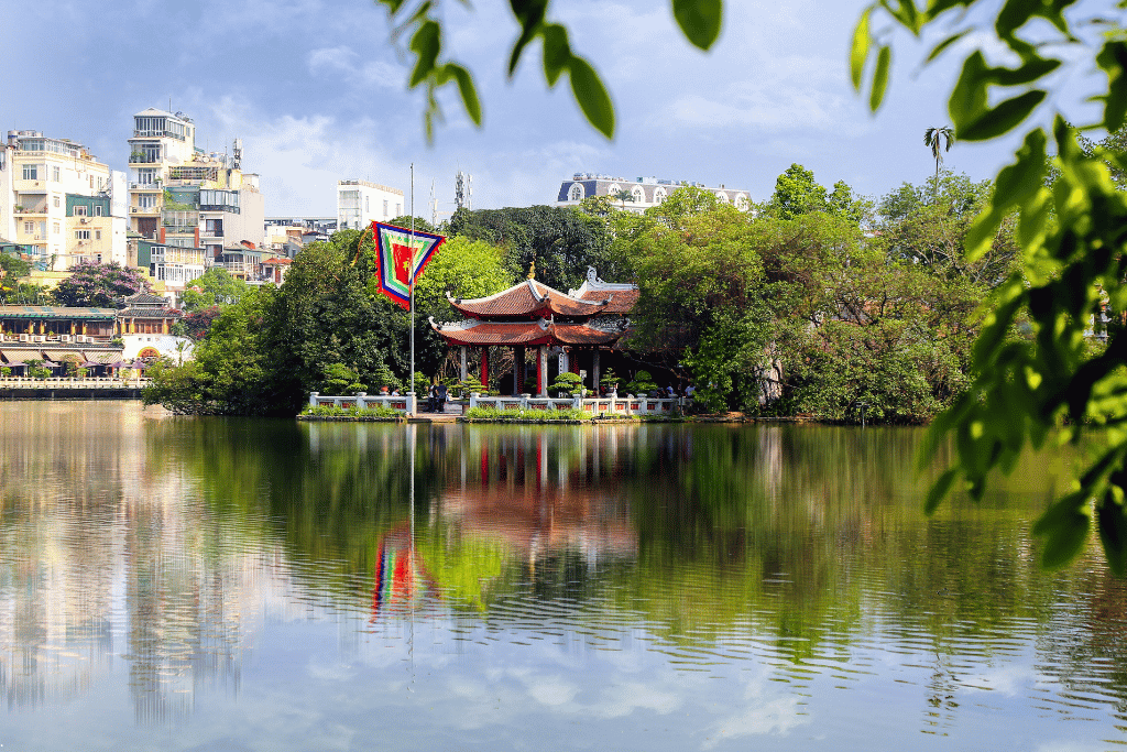 Red-roofed lakeside pavilion and Vietnamese flag mirrored in still green water