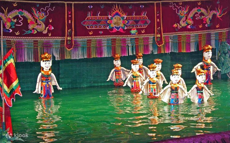 Costumed wooden water puppets moving across a green pool before an embroidered red backdrop