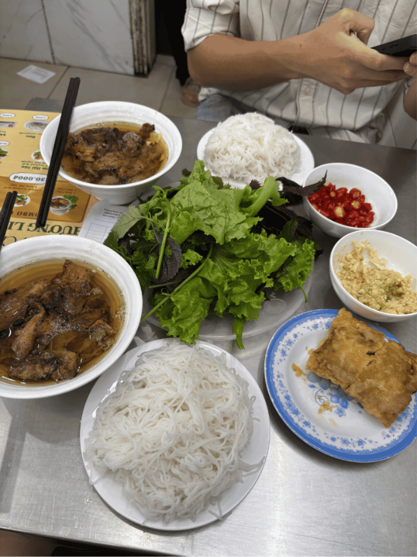 Bowls of grilled pork in broth with rice vermicelli, fresh herbs, chilli and a fried spring roll