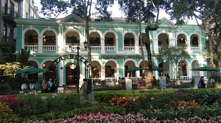 A restored mint-green colonial villa, now a Starbucks, framed by garden flowers on Shamian Island