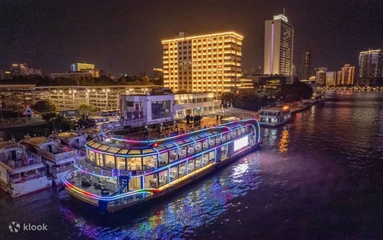 A neon-lit cruise boat on the Pearl River passing illuminated buildings at night in Guangzhou