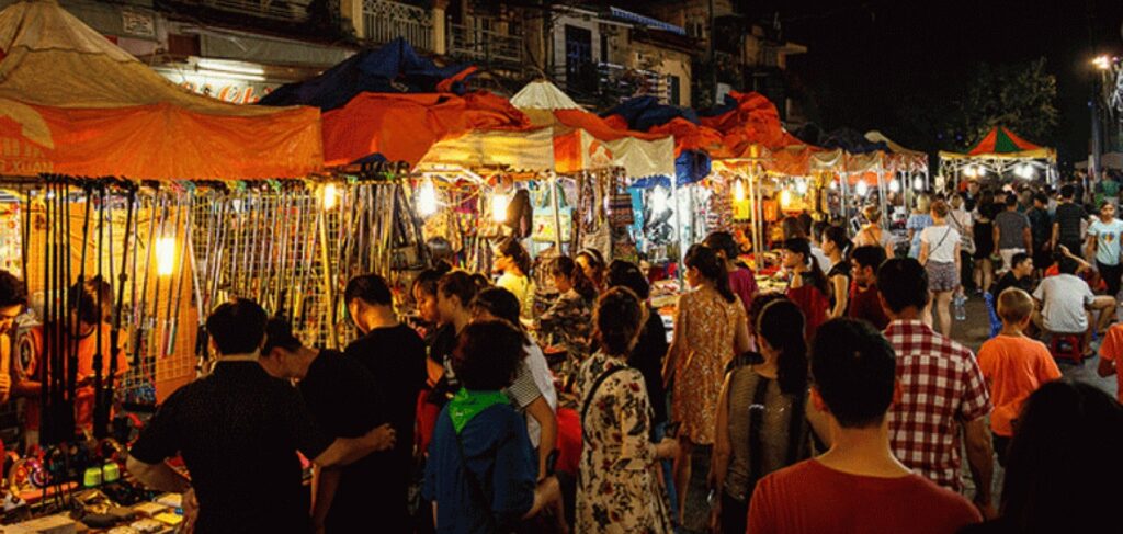 Crowded night market stalls lit up along a closed-off Hanoi street