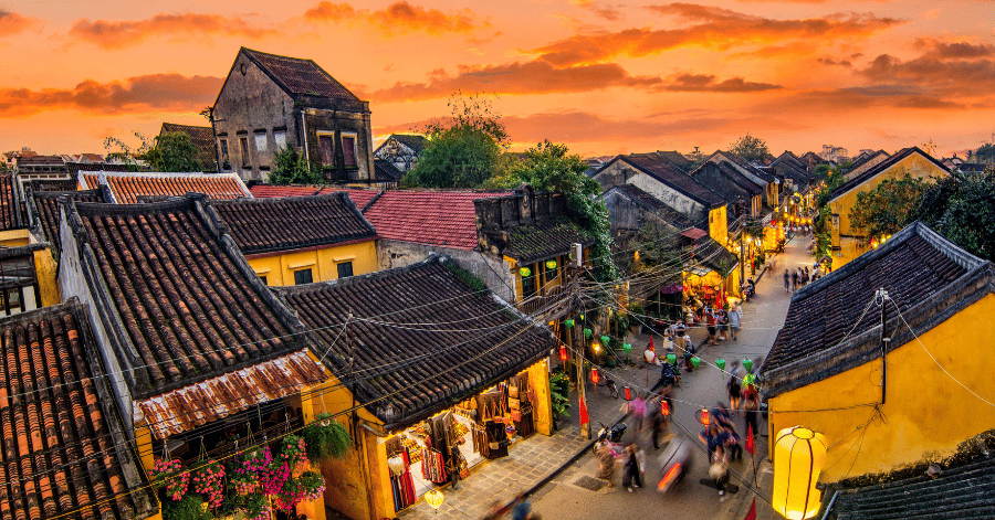 Tiled rooftops and lantern-lit lanes of a Vietnamese old town under an orange sunset