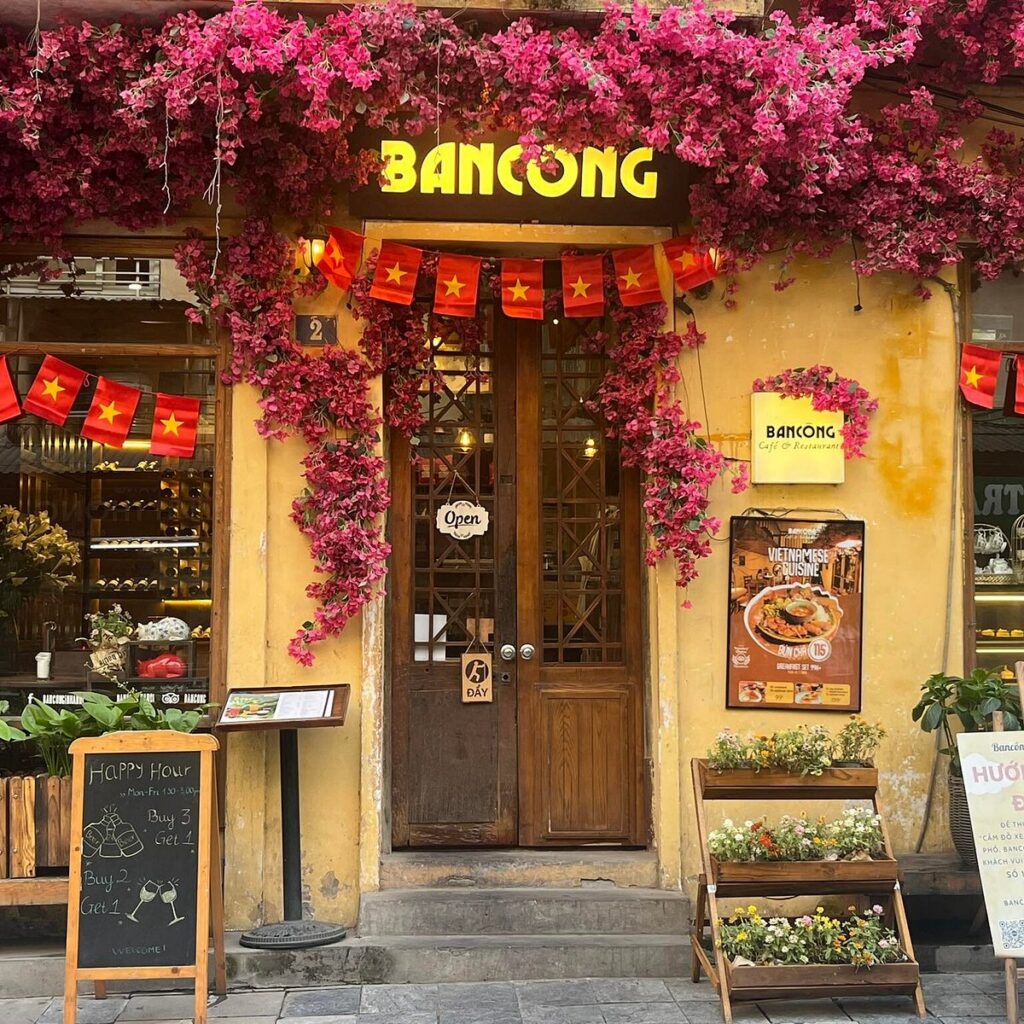 Yellow colonial shopfront of Bancong Cafe draped in magenta bougainvillea and flag bunting