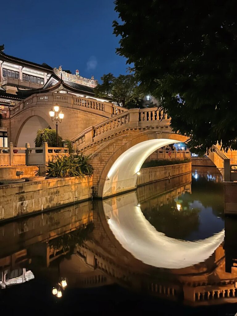 The illuminated Moon Bridge at Yong Qing Fang reflecting in the water to form a full-moon circle at night