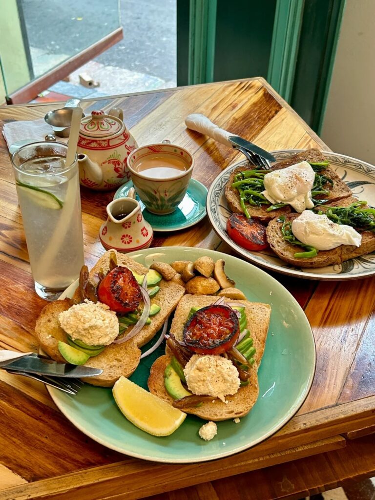 Avocado toast and poached eggs on greens with a floral teapot on a wooden table