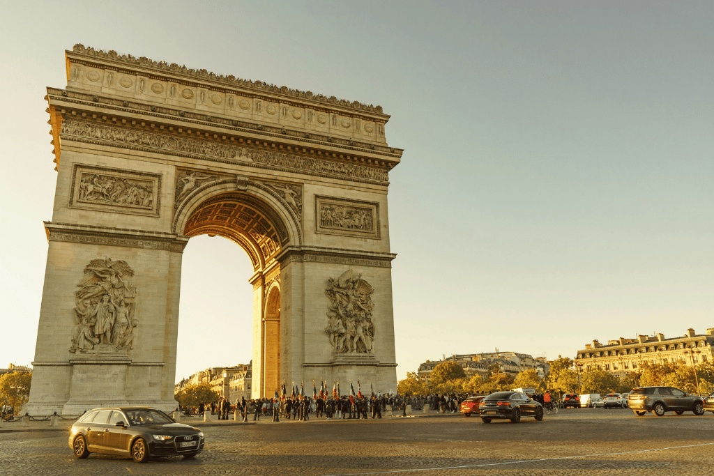 Arc de Triomphe illuminated at golden hour with crowds and traffic circling below